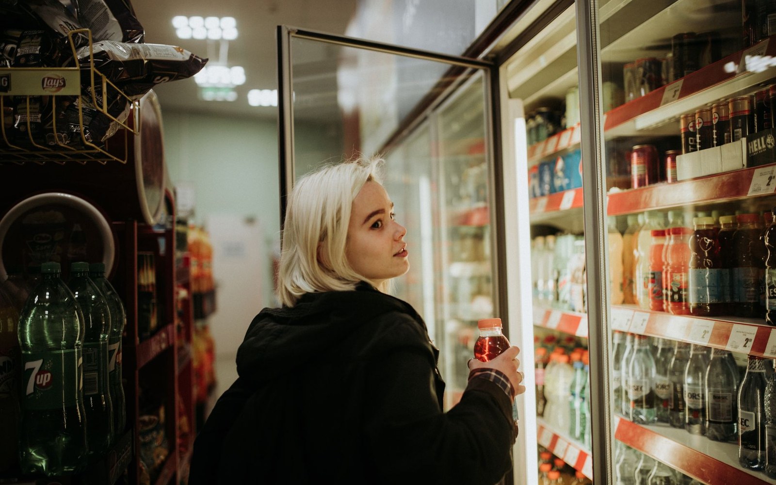 Woman with blonde hair selects a bottled drink from a convenience store cooler